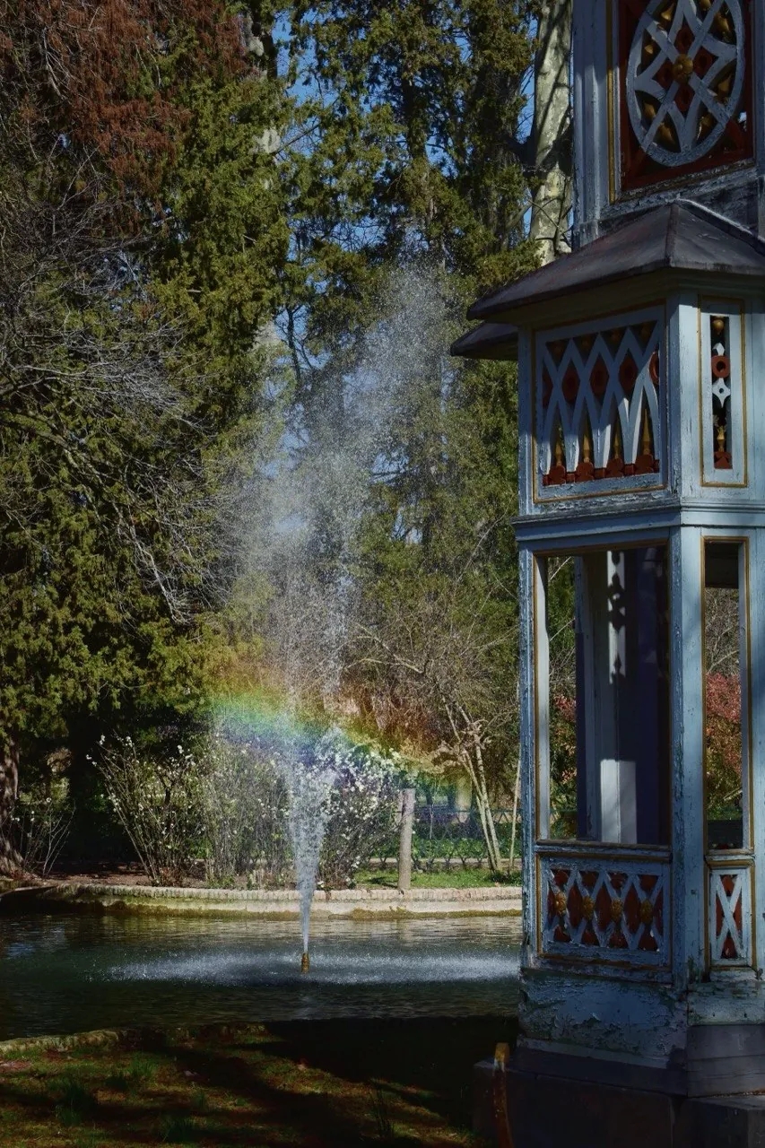 Fuente con un arcoíris junto a un templete en un parque