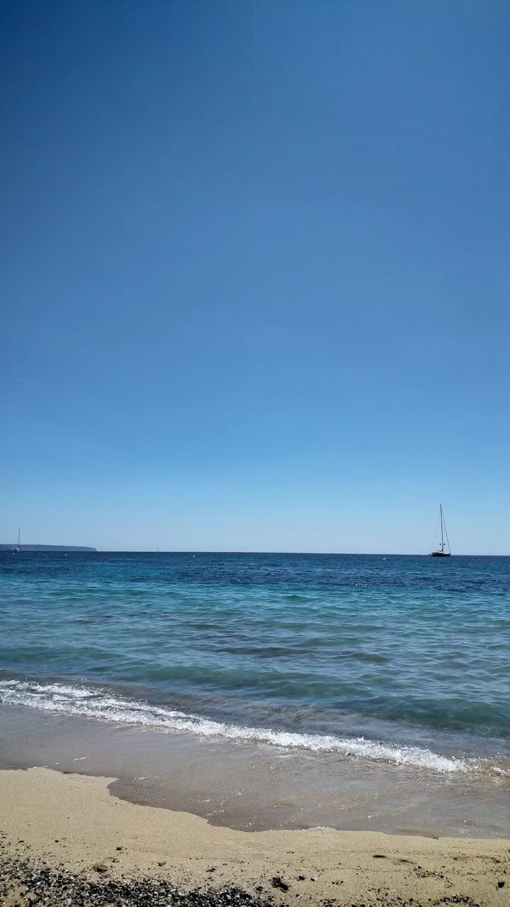 Playa con un velero en el horizonte