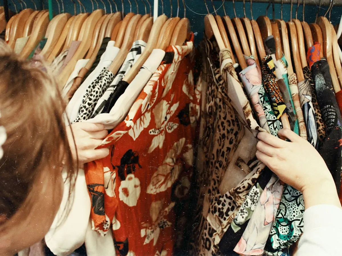 Manos buscando entre ropa colgada en perchas